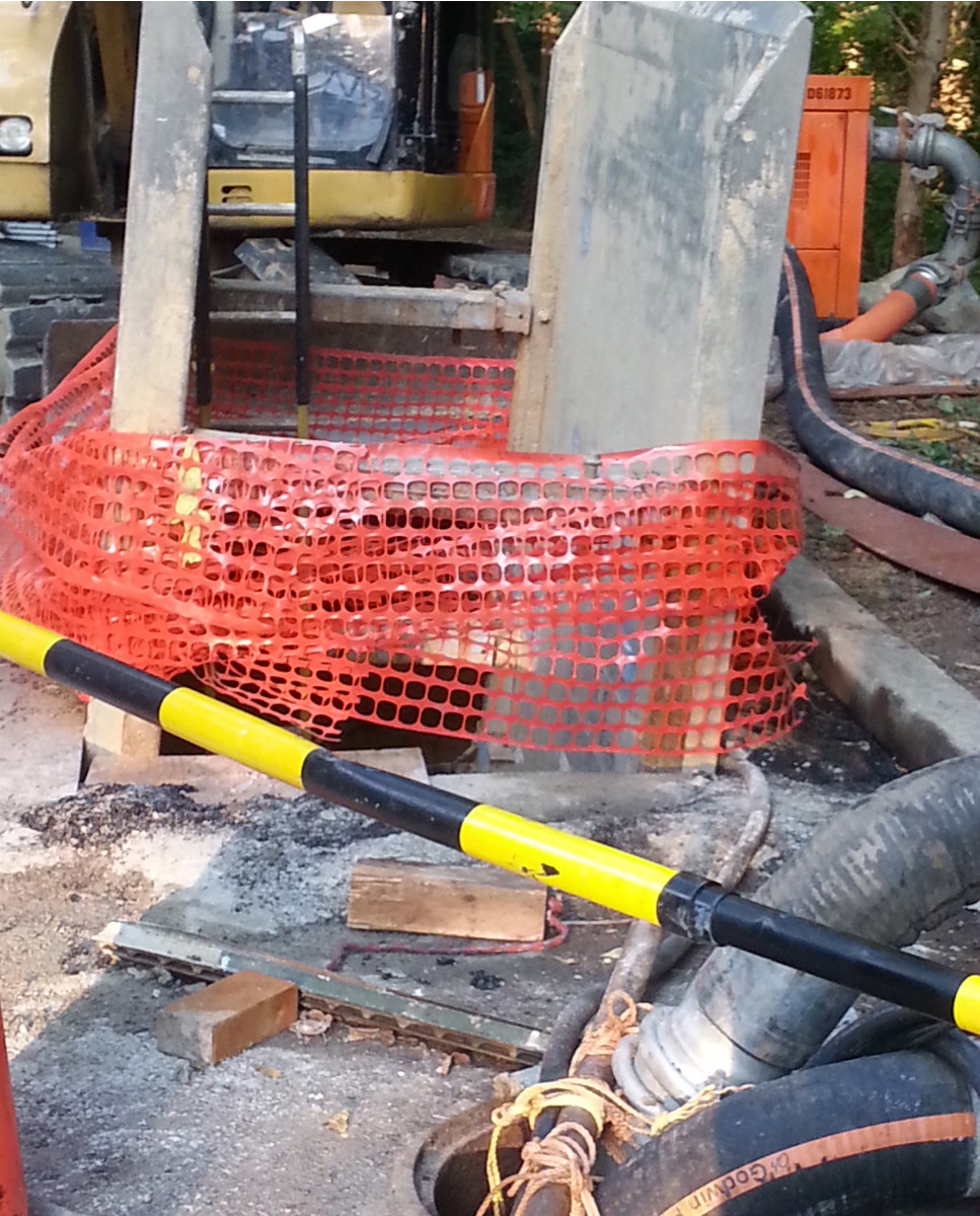 In the foregound are both bypass hoses. In the background is one of the bypass pumps. And in the center - just downstream from the manhole - are two concrete shoring panels and orange construction fencing for the work pit. (photo by Marjorie Share)